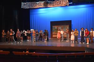 about 20 students are on stage in casual dress performing below a welcome wildcats sign